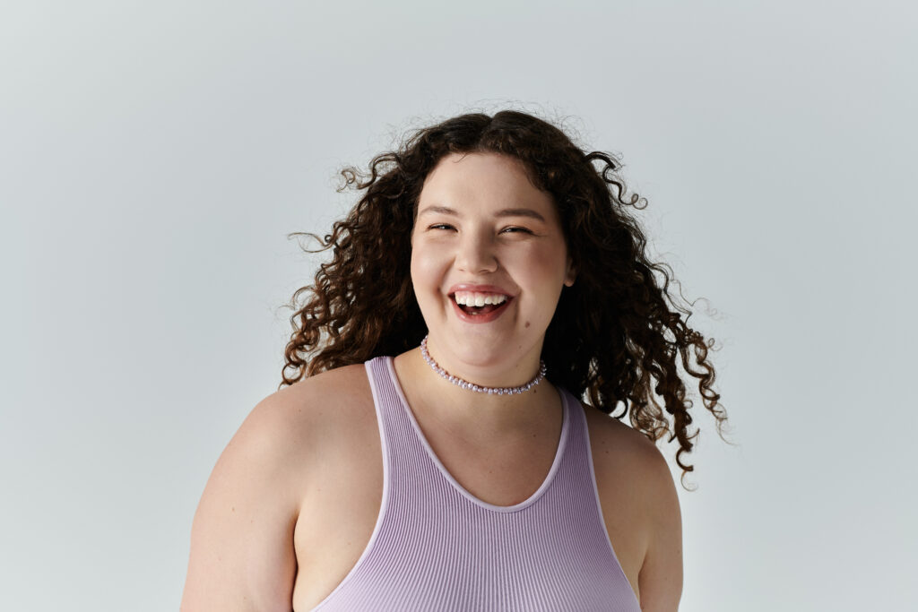 Confident woman smiling in lilac top, symbolizing skin rejuvenation with GHK-Cu peptides