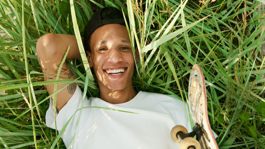 Smiling young man lying in grass with skateboard, symbolizing health and vitality