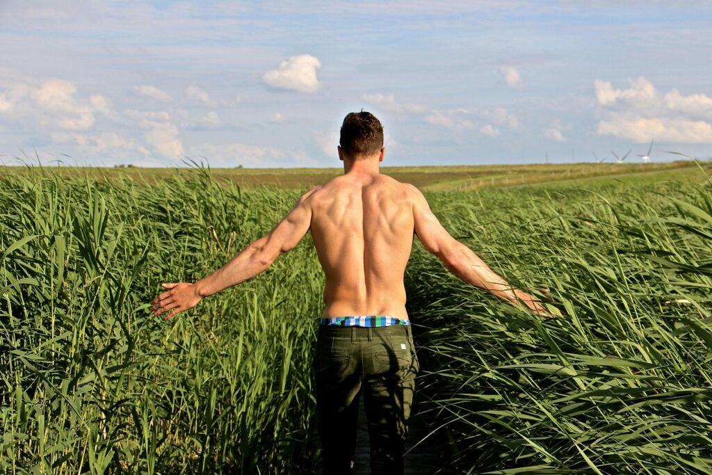 Fit man walking shirtless through tall grass, back muscles visible, symbolizing strength and vitality